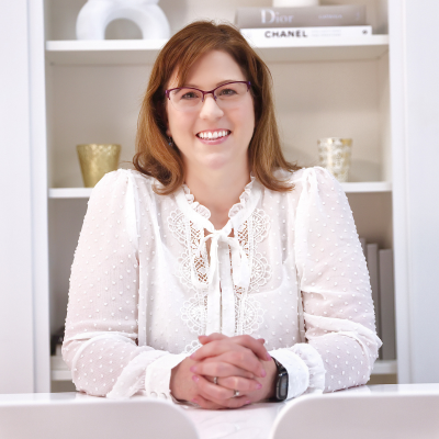 Photo of Elizabeth Kelly - a smiling, white woman with brown hair wearing a white blouse, sitting at a desk